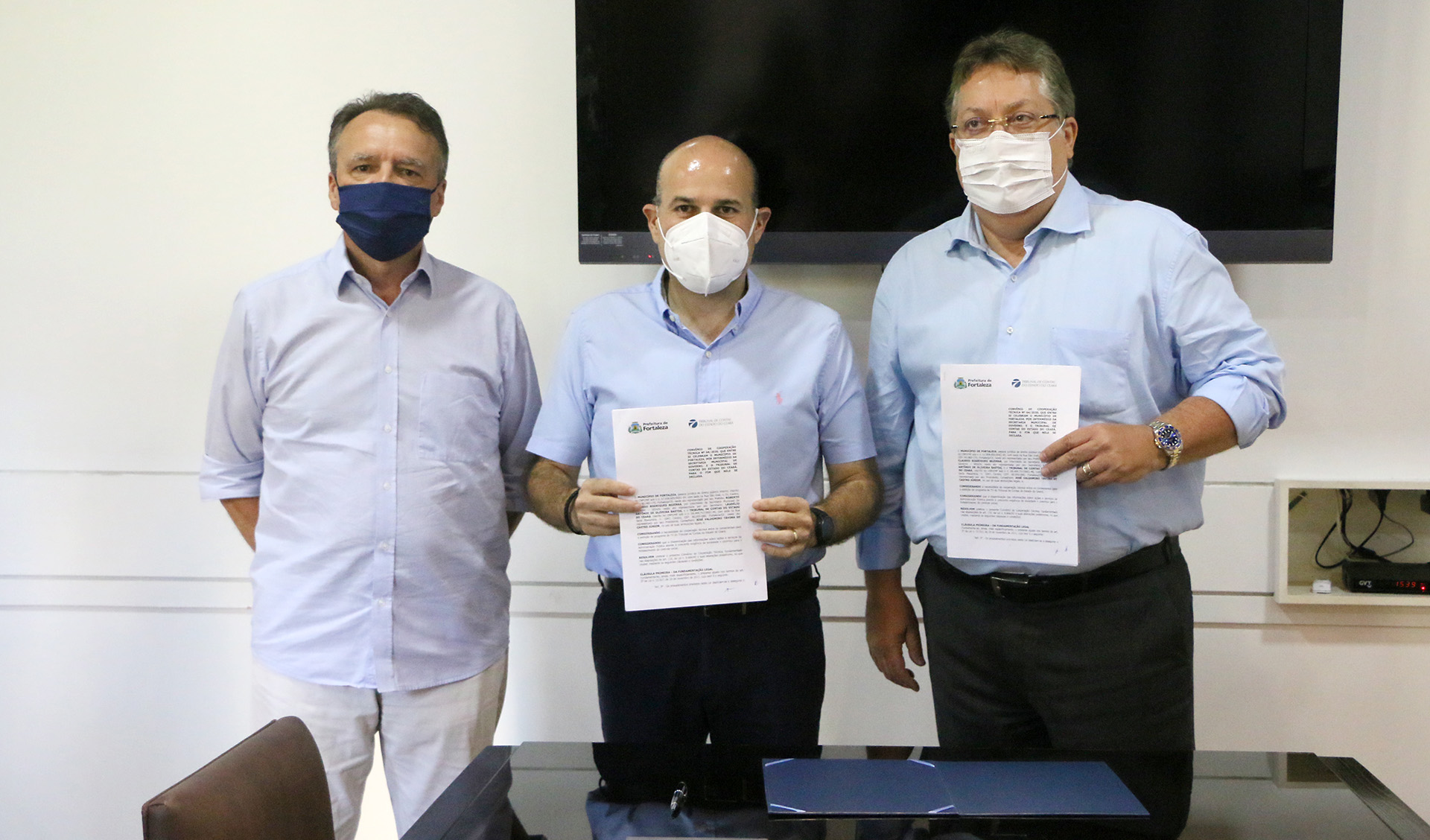 prefeito em pé ao lado de dois outros senhores, todos de máscara posando para a foto. prefeito segua um documento e mostra para a foto